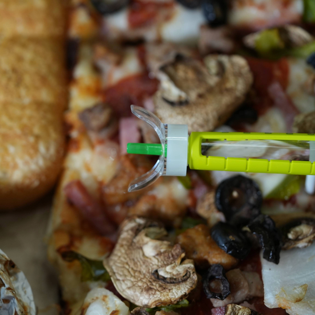 Steady Shot large size attached to 6mm insulin pen needle with pizza in the background. Perfect for diabetics managing insulin injections and enjoying balanced meals. Ideal for diabetes meal prep and injection site rotation.
