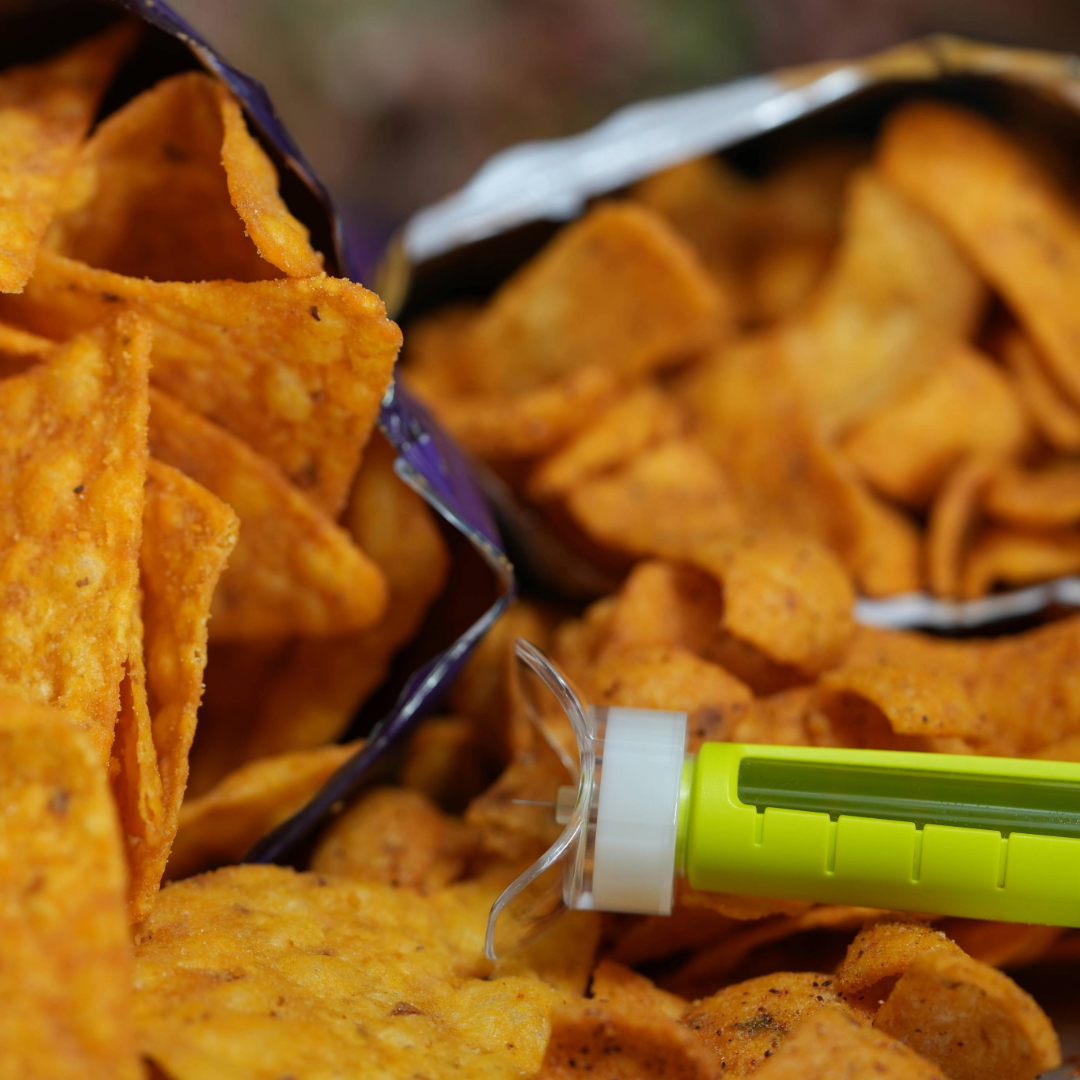 Steady Shot small size attached to 4mm insulin pen needle with Doritos and Fritos in the background. Reusable diabetes tool for easy injection site rotation, perfect for managing diabetes during snack time or meal prep.